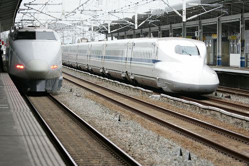 An N700 Series Nozomi train passes by a 100 Series Kodama train stopped at a station