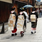 Вот сзади особенно хорошо видно. Первые две девушки (дальше от нас) - гэйко. Одна в парадном черном кимоно и парике, а другая - просто в летнем полу-формальном кимоно. За ними - две майко, обе старшие, если судить по прическам