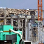 Рабочие в защитных костюмах и масках на крыше здания 4-го реактора АЭС «Фукусима-1», 20-е февраля 2012 г. Окума, префектура Фукусима. Жёлтая область (в левой части здания) это верхушка защитной оболочки реактора. Зелёное (в правой части здания) — дозаправочное оборудование