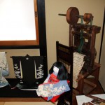 Кукла итимацу-нингё в фурисодэ сидит спиной к миниатюрному ткацкому станку